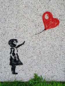 a balloon in form of a heart flies away. a child sends it away